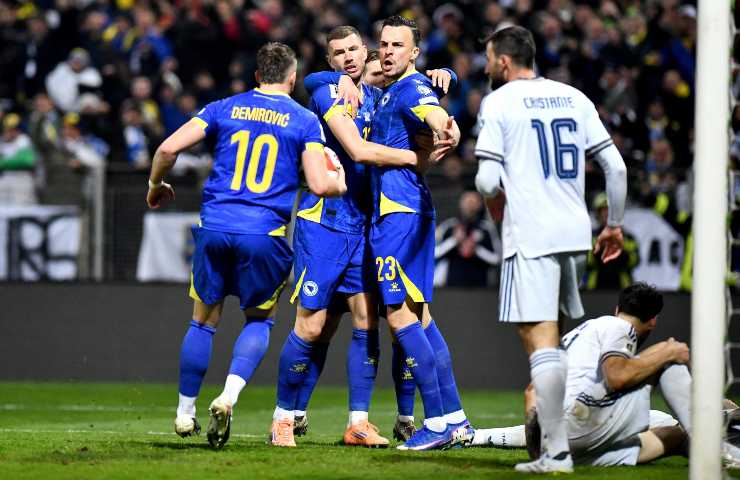 Calciatori della Bosnia in tenuta da gioco blu festeggiano mentre alcuni giocatori dell'Italia hanno una espressione delusa in campo.